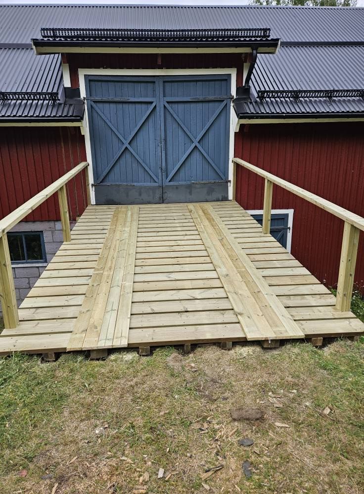 Nybyggd lobrygga i trä framför en röd lada